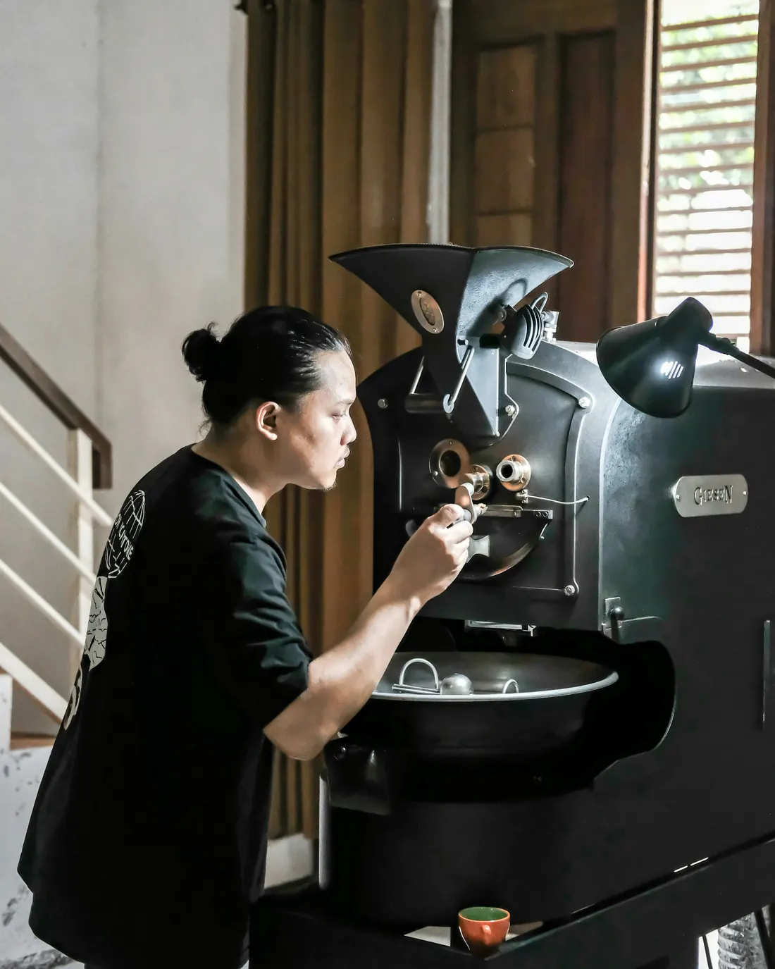 A coffee roaster checking a batch at the roasting machine in daylight